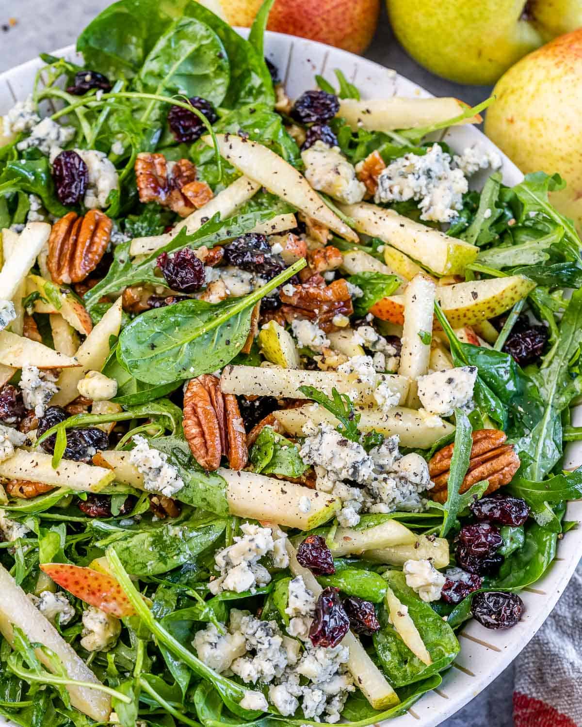 Closer view of Arugula Pear salad, highlighting the balance of ingredients like blue cheese and dried fruit.