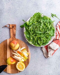 Cutting board with whole pears, sliced pears, and a lemon next to a bowl of arugula.