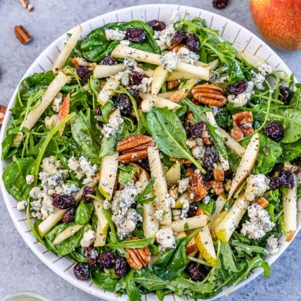 Top view of arugula salad with pears, blue cheese, and pecan, in a round bowl.