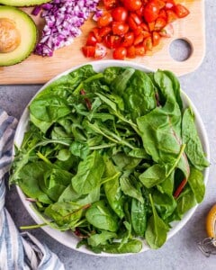 A large bowl filled with fresh spinach, chopped tomatoes, and sliced avocado, ready to be assembled into a salad.