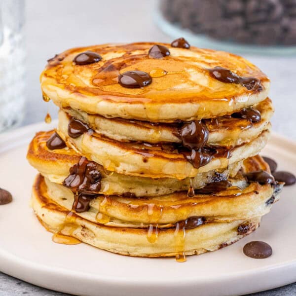 Stack of chocolate chip pancakes on a plate with a drizzle of maple syrup.