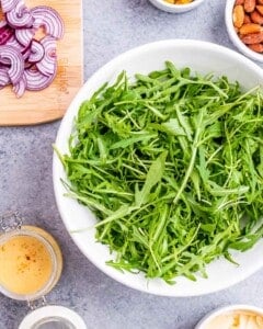 Just the arugula in a white bowl, sitting on the counter next to a small jar of vinaigrette.