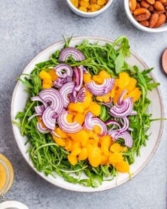 Salad bowl filled with fresh arugula, topped with mandarin segments and thinly sliced red onion.