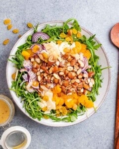 Bowl of salad before tossing, with toppings like almonds, onion, and mandarins added on top of the greens.