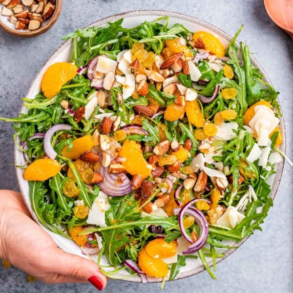 A hand holding the fully assembled salad in a white serving bowl, showing off the bright colors and textures.
