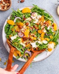 Salad being gently tossed with wooden utensils to mix the dressing and ingredients evenly.