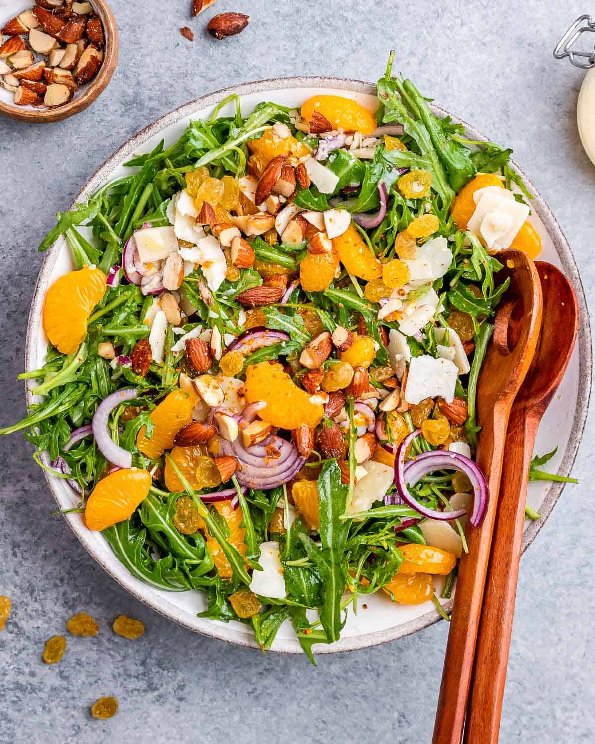 Wooden salad servers beginning to toss the ingredients together in the bowl of mandarin orange salad.