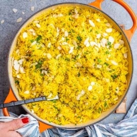 Fluffy yellow rice in a pot with almonds and parsley mixed throughout.