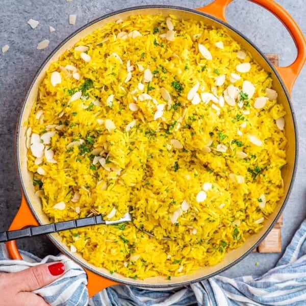 Fluffy yellow rice in a pot with almonds and parsley mixed throughout.
