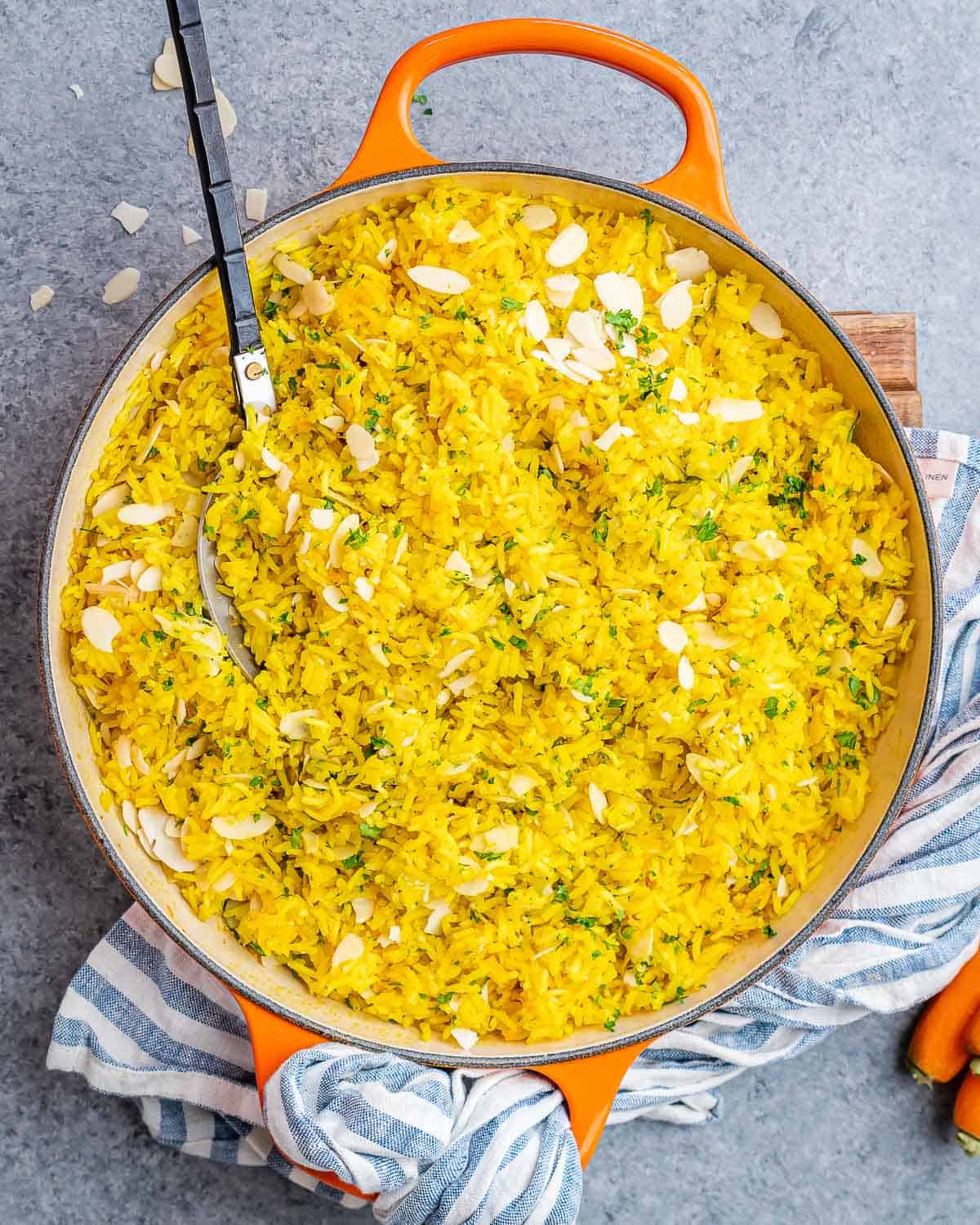 Cooked yellow rice in a pot with toasted almonds and chopped parsley on top, ready to serve.