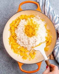 Basmati rice being stirred into sautéed onion, carrot, and garlic mixture in the pot.
