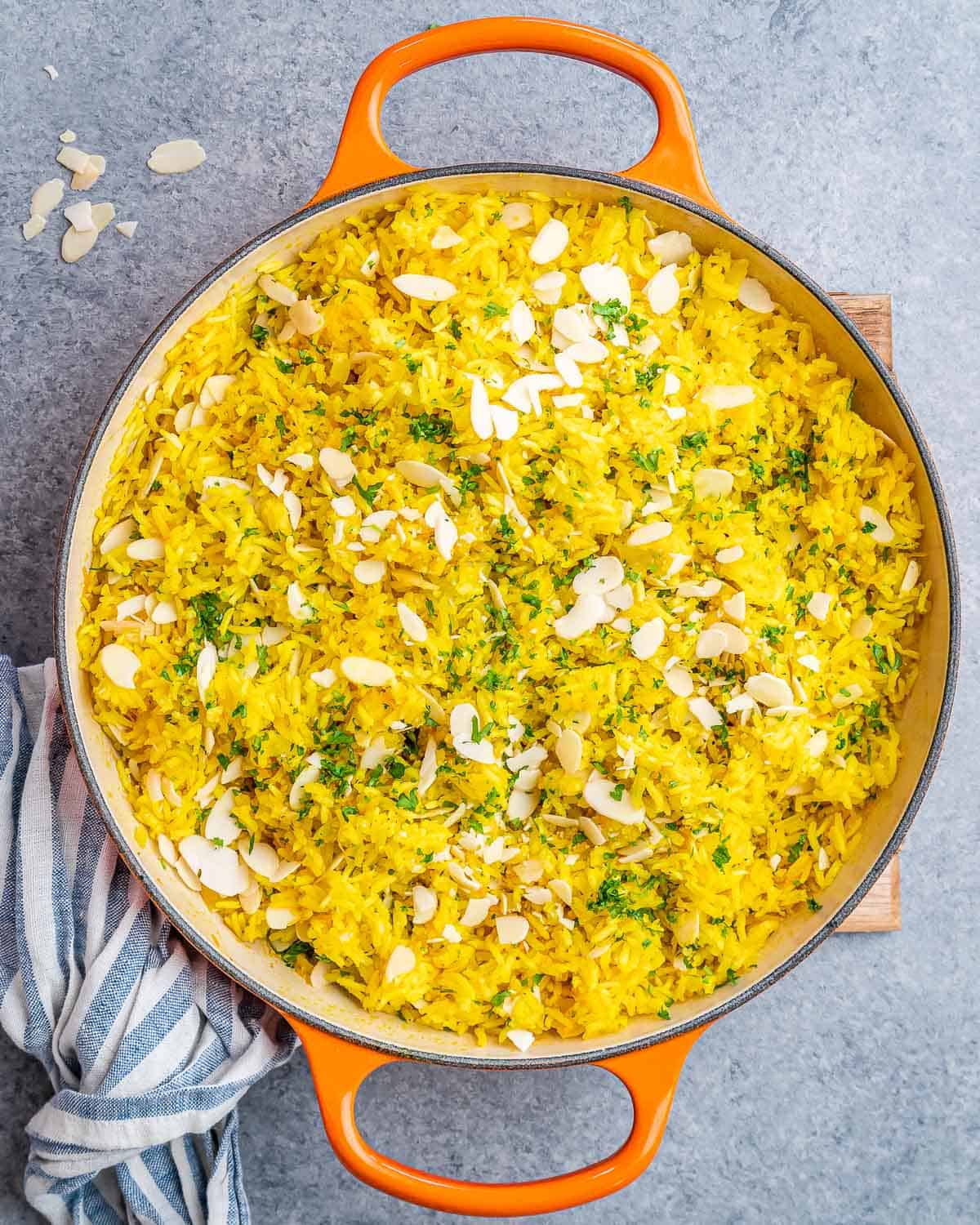 Overhead shot of golden yellow rice garnished with fresh parsley and almonds.