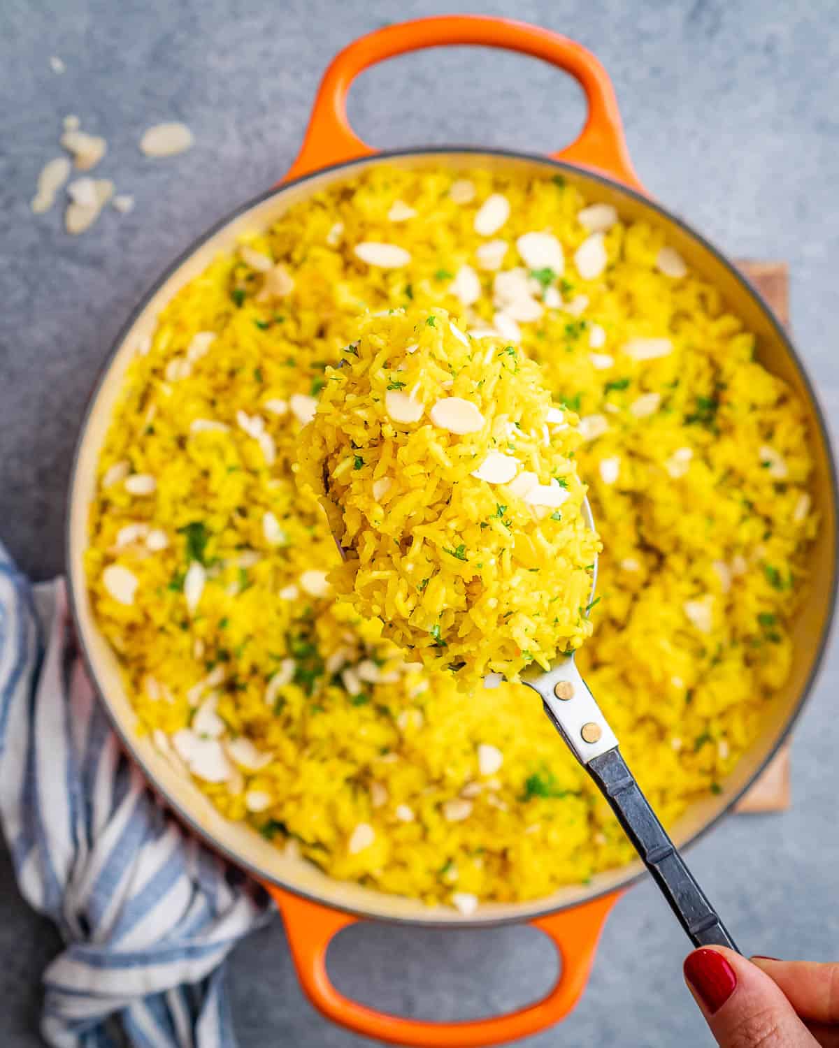 Ladle scooping a serving of yellow rice with almonds and parsley from the pot.