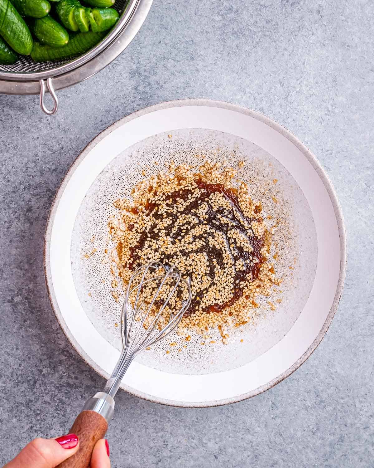 Using a whisk to mix soy sauce, rice vinegar, sesame seeds and sesame oil.