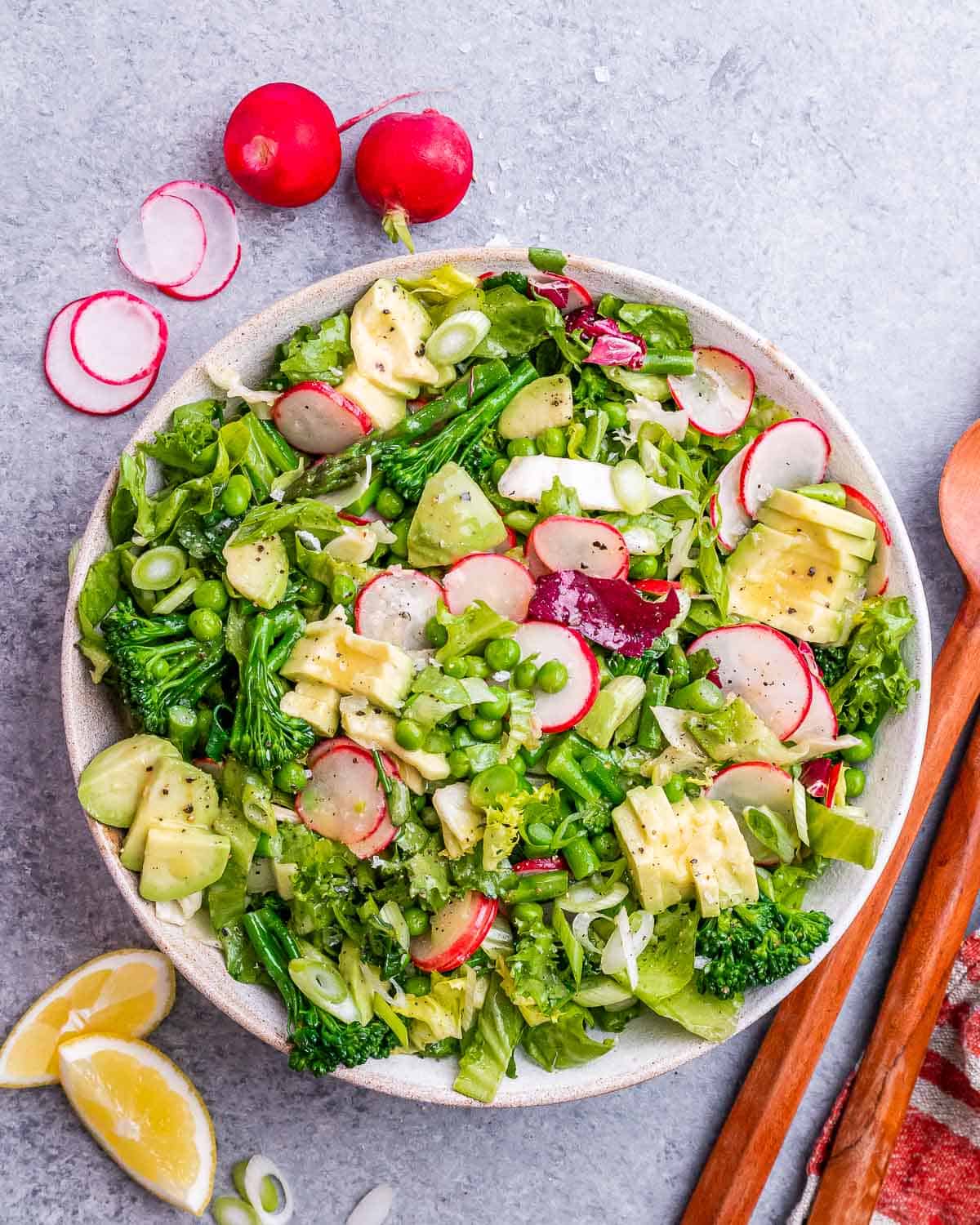 A bowl of spring mix salad topped with radishes, broccoli, asparagus and peas.