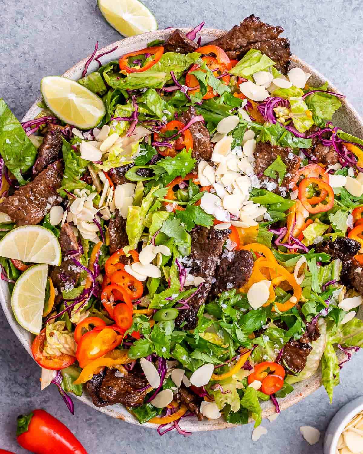 Thai beef salad in a white bowl with lime, peppers and almonds.