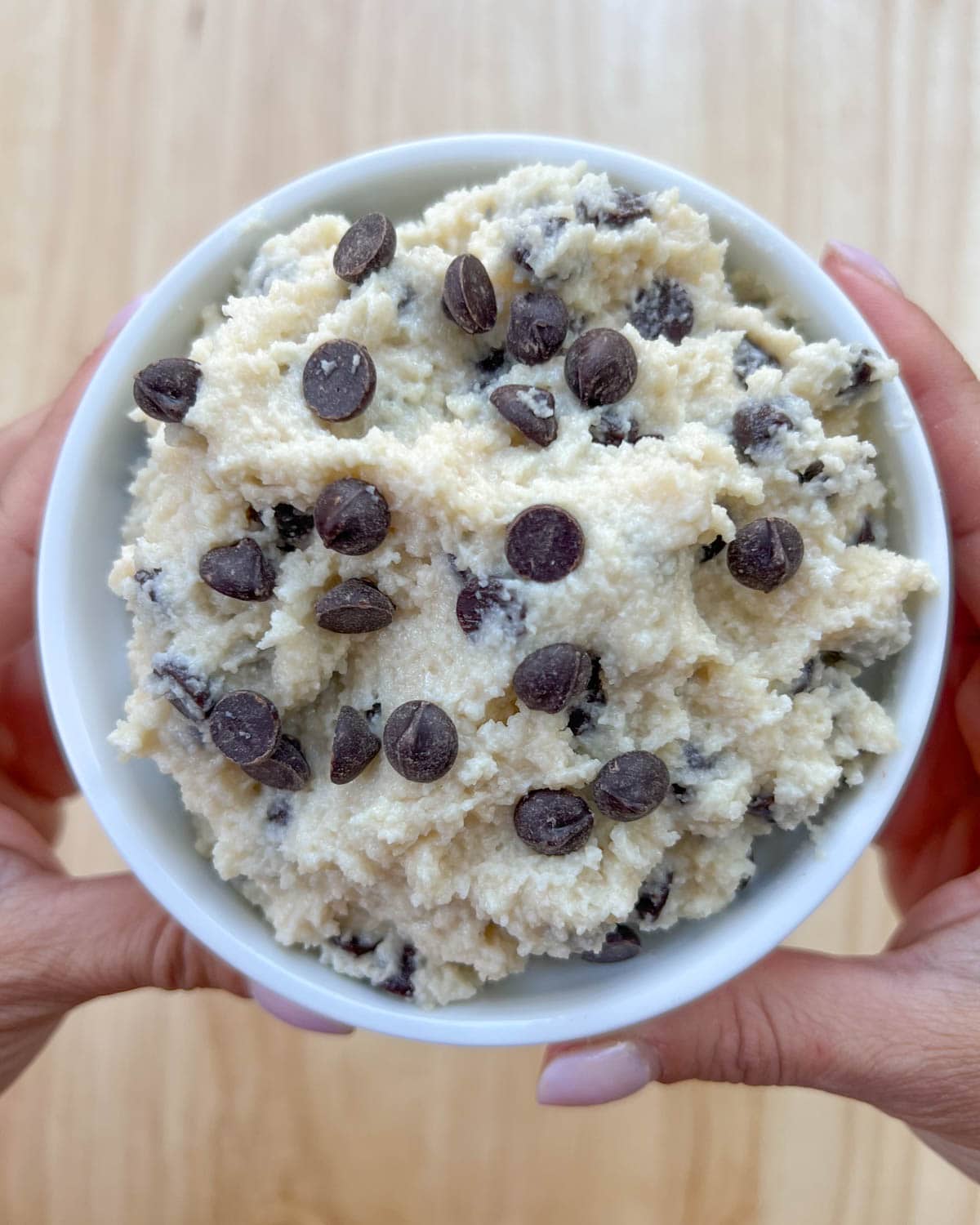 a hand holding a bowl of edible cookie dough.