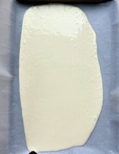 batter poured onto a sheet pan lined up with parchment paper.