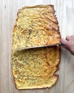 baked cottage cheese wrap on a cutting board with knife slicing it in middle.