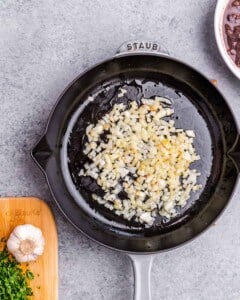 Diced onion and garlic being sautéed in a skillet, part of the filling prep.