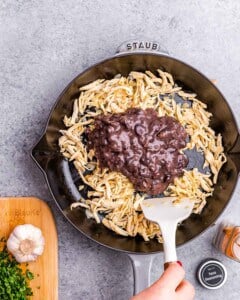 A skillet with shredded chicken and mashed black beans being mixed together with a spatula.