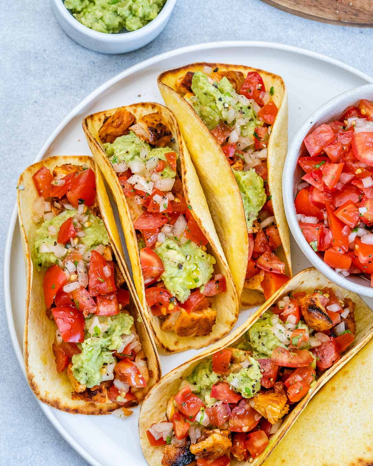 Close-up of four tacos filled with grilled chicken, guacamole, and tomatoes in warm corn tortillas.