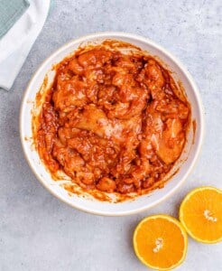 Chicken thighs marinating in a bowl of orange-tinted sauce made from tomato paste, citrus juice, garlic, and taco seasoning.