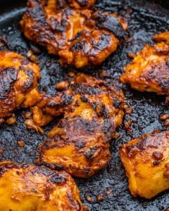 Marinated chicken thighs cooking on a grill pan, with a smoky char forming on the outside.