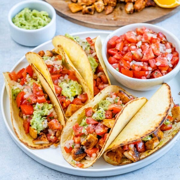 Chicken street tacos fully assembled with diced chicken, salsa, and guacamole, served on a white plate.