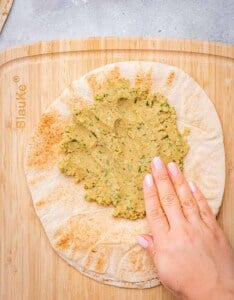 hand spreading falafel mixture over pita bread.