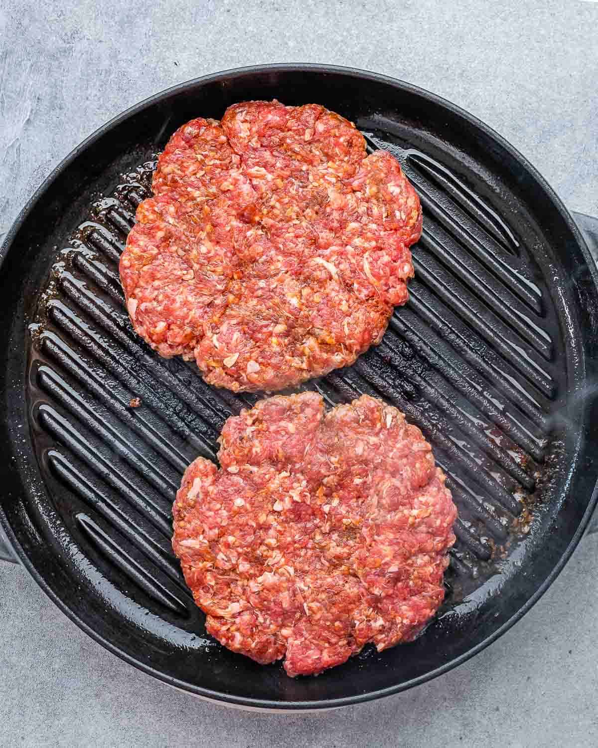 Raw ground beef patties cooking on a grill pan.