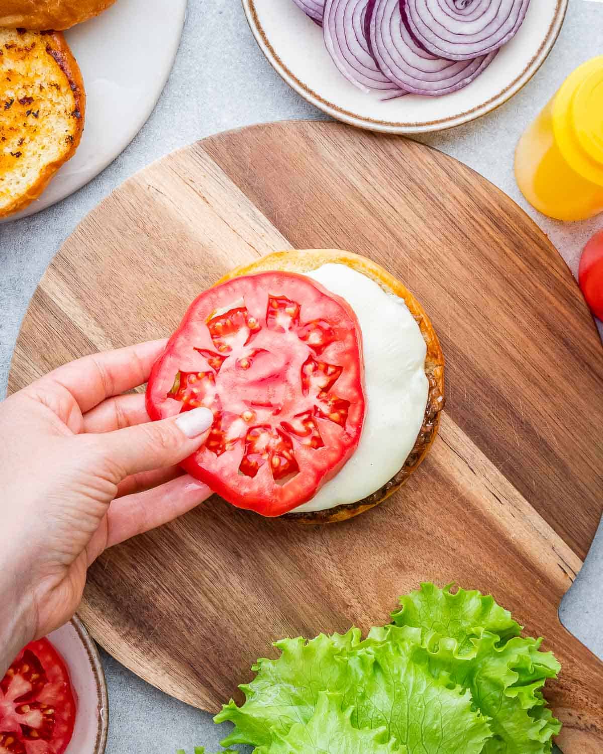 Adding a tomato slice over a bun with cheese.