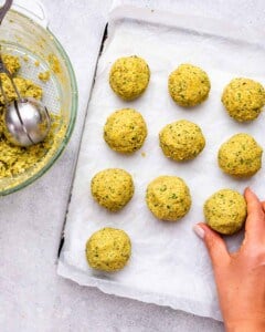 Baking sheet lined with parchment paper holding uncooked falafel balls before frying.