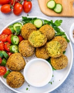 Platter of falafel balls with fresh vegetables and a bowl of creamy tahini sauce for dipping.