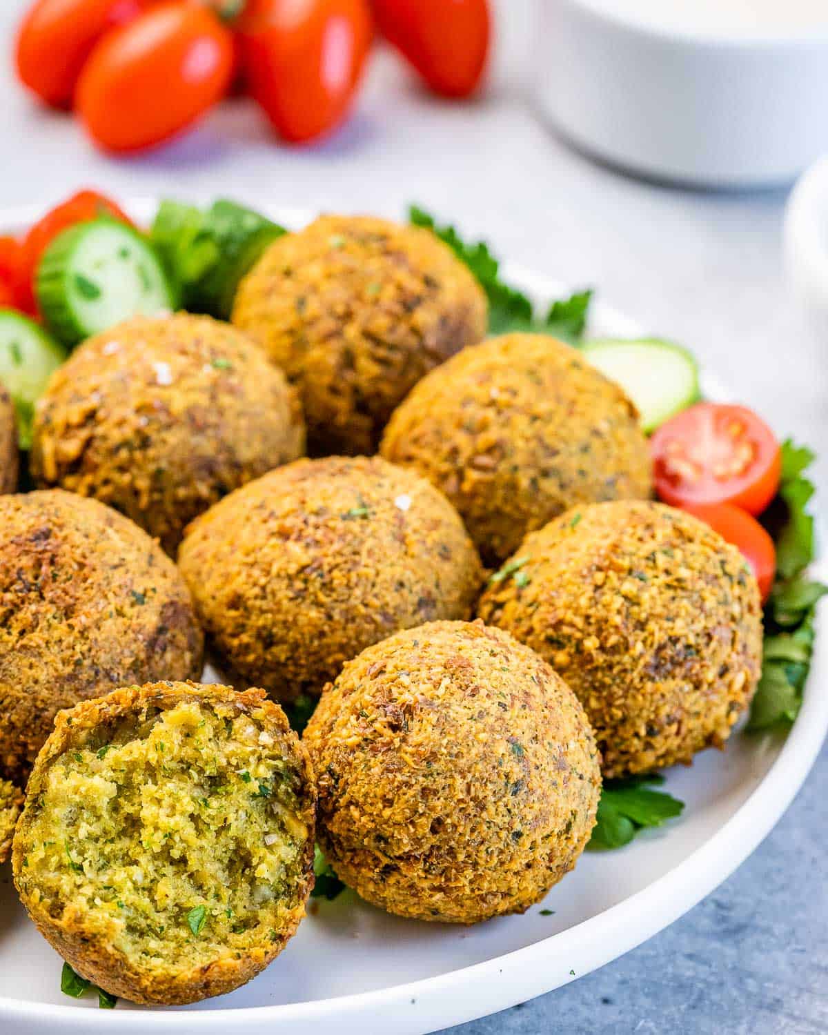 Close-up of golden-brown fried falafel balls piled on a plate with fresh cucumber and tomato slices.