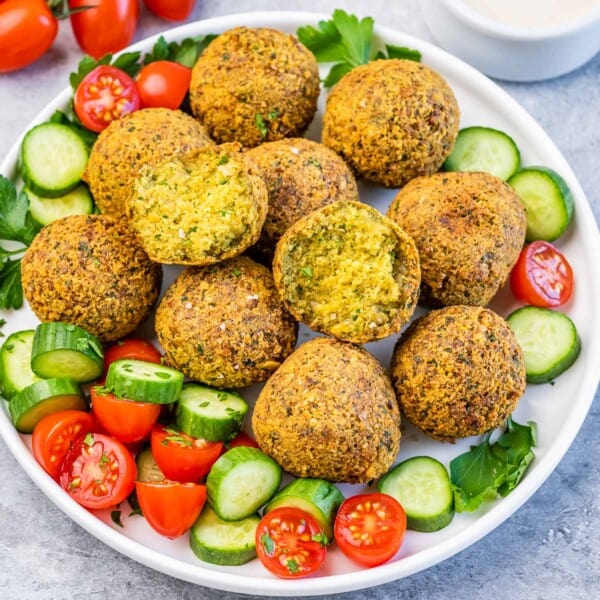 Freshly fried falafel balls on a plate with cucumber slices, cherry tomatoes, and parsley garnish.