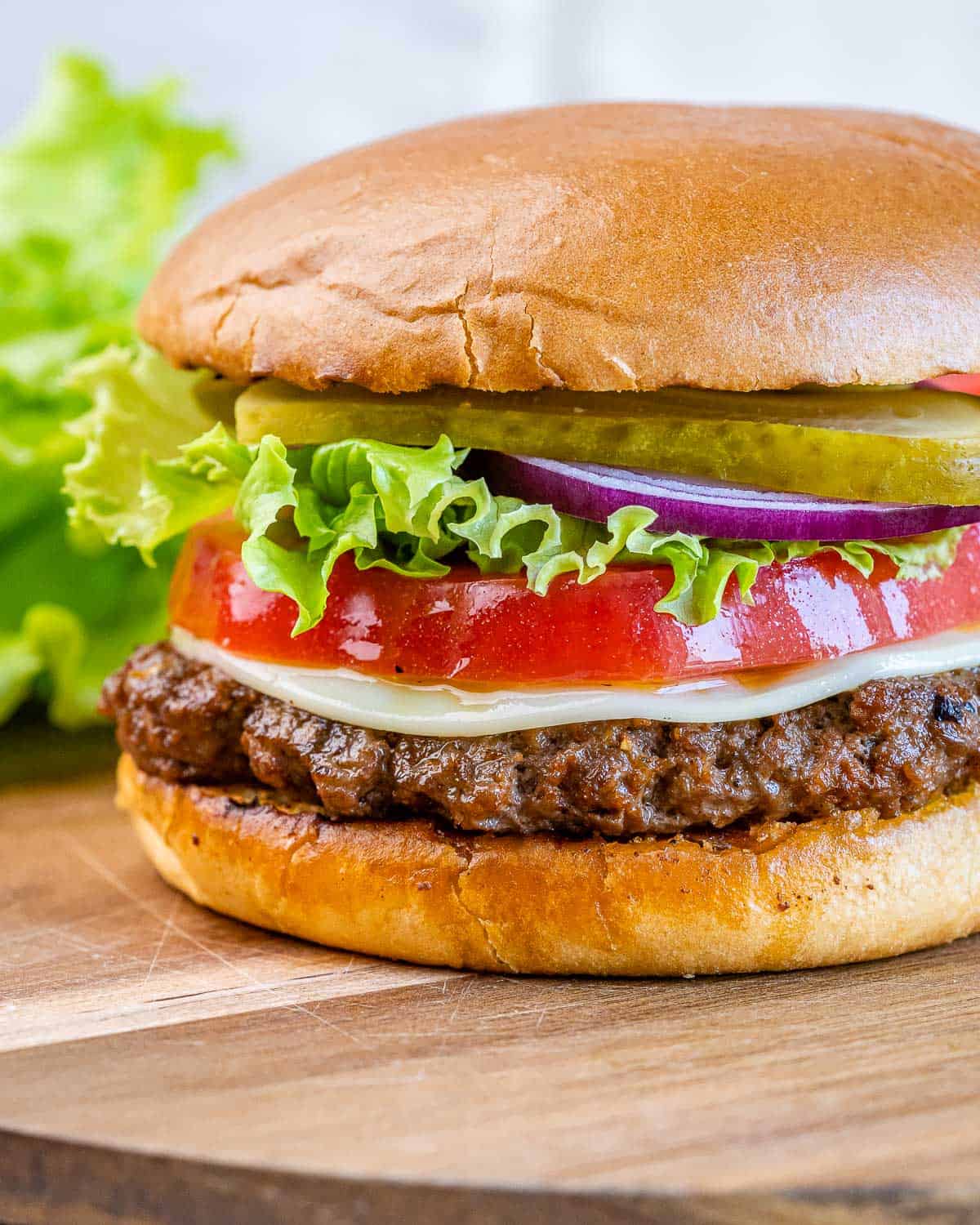 Homemade hamburger with cheese, tomato slice, lettuce, red onion and pickles.