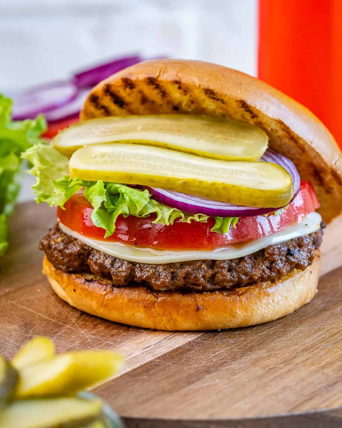 hamburger with top bun slightly off showing the patty, lettuce, tomatoes, and pickles.