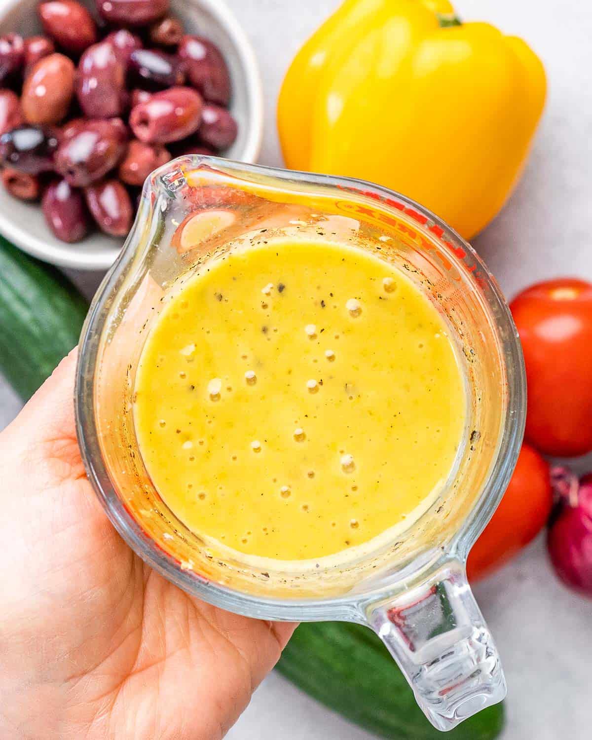 Lemon dijon dressing in a pyrex measuring cup being held up by someone.