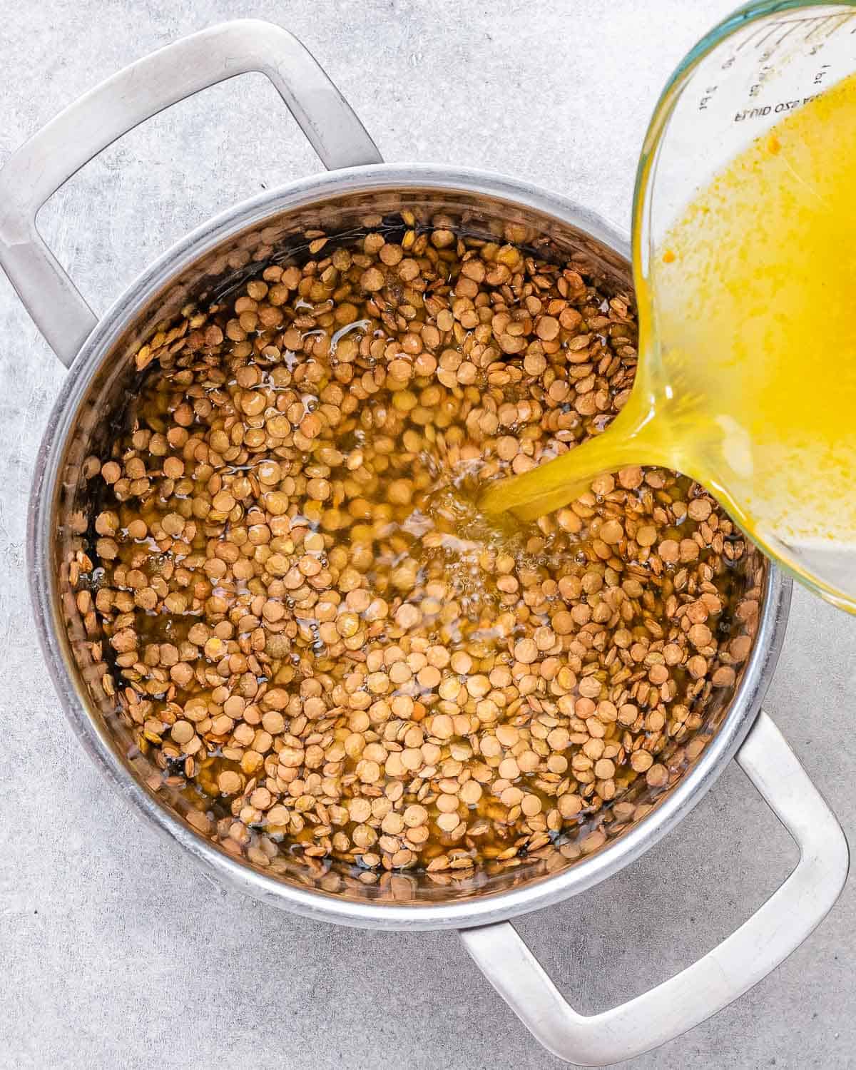 Pouring broth into a pot with lentils.