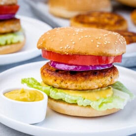 A salmon burger on a white plate with a small bowl of mustard.