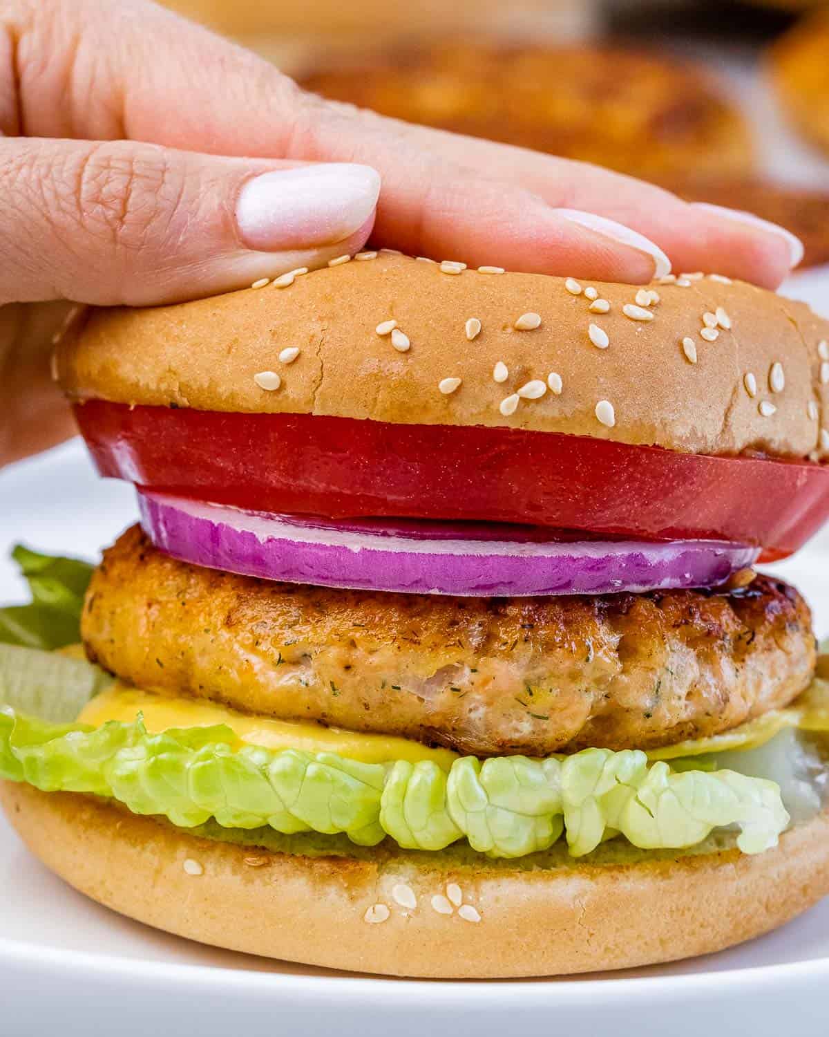 hand pressing down on a salmon burger on a plate.