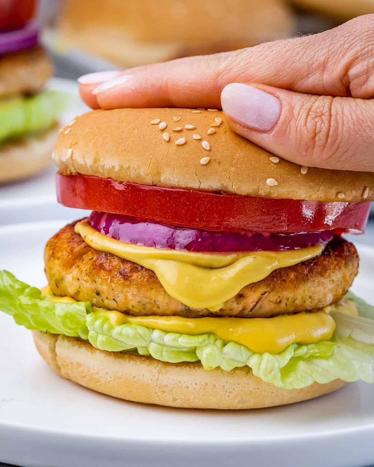 Woman's hand topping a salmon burger with a bun on top.