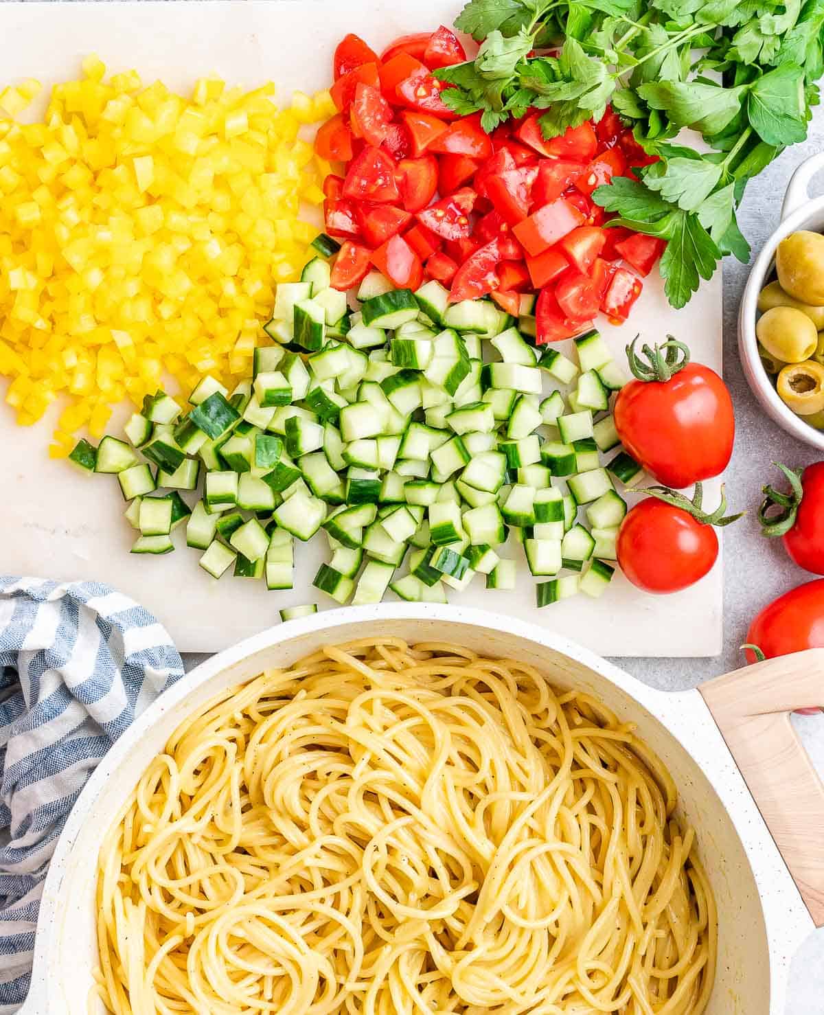 a bowl of cooked spaghetti and chopped veggies on a platter.