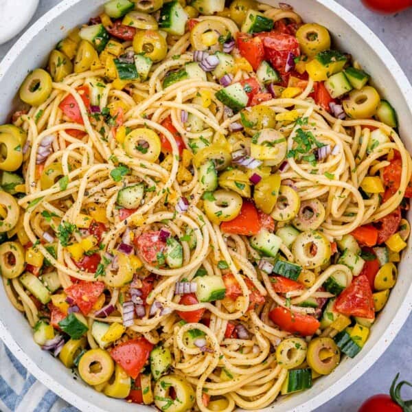 spaghetti salad with veggies and olives in a round white bowl.