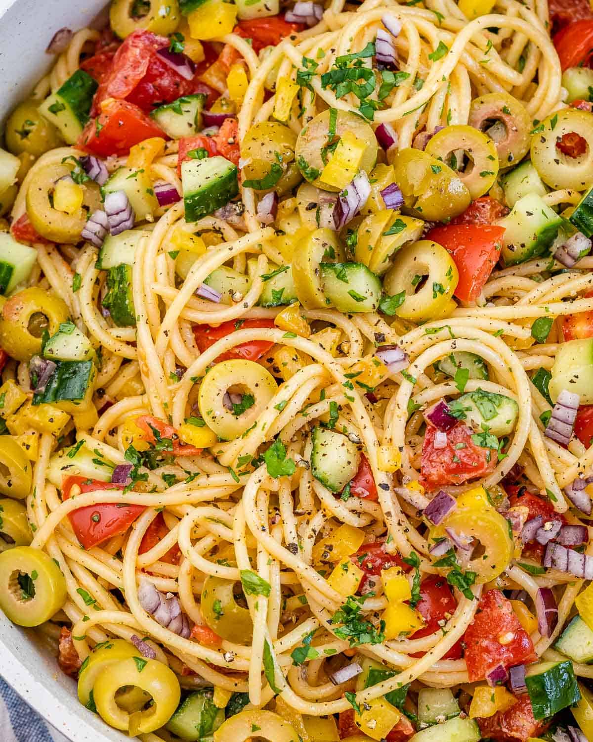 spaghetti salad in a dish made with a variety or veggies including sliced green olives.