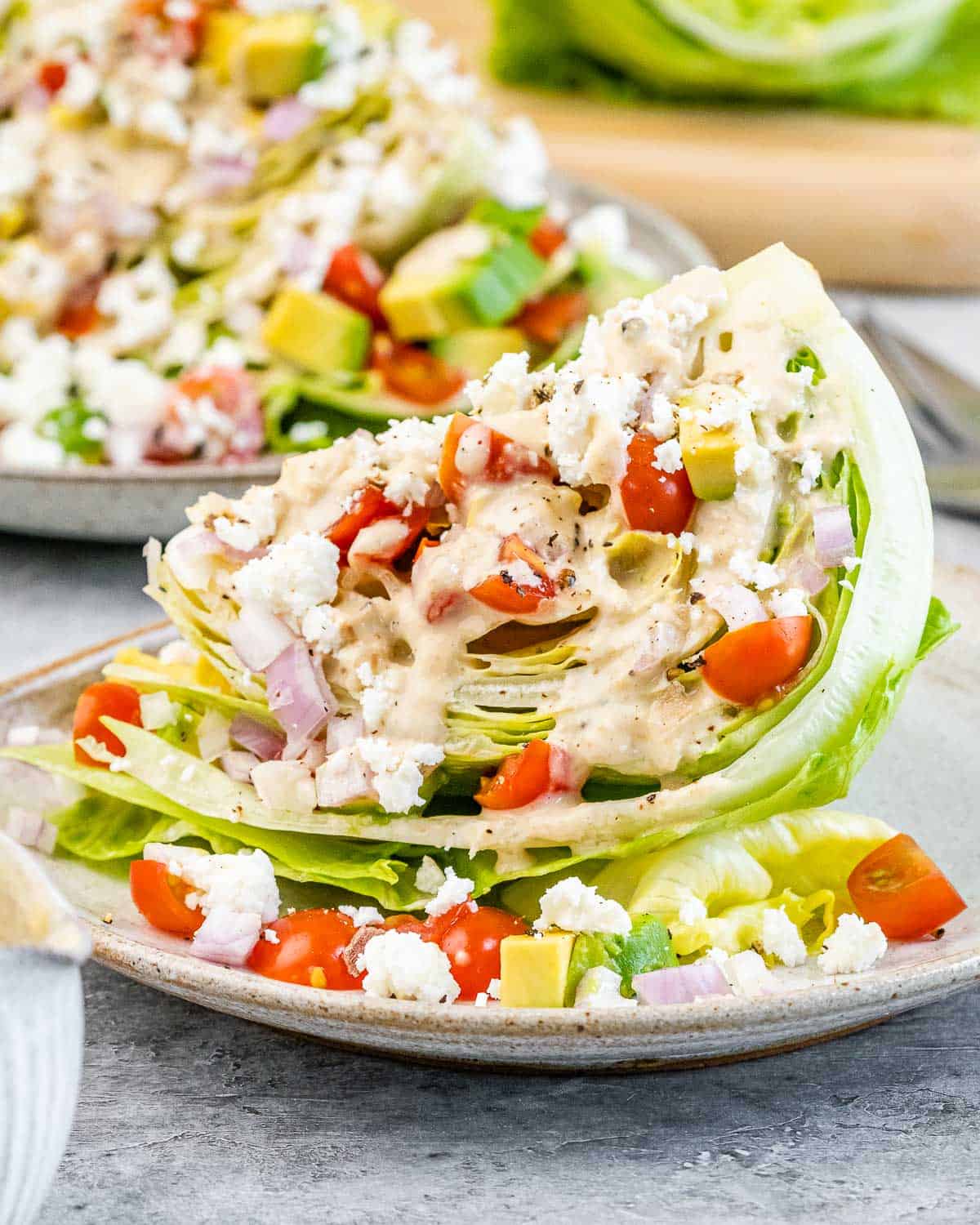 A wedge salad on a plate topped with dressing and chopped tomatoes.