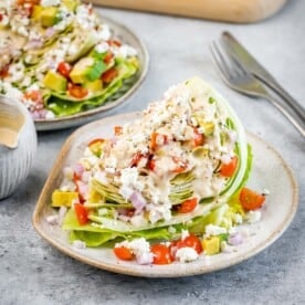 A wedge salad on a plate topped with dressing and chopped tomatoes.