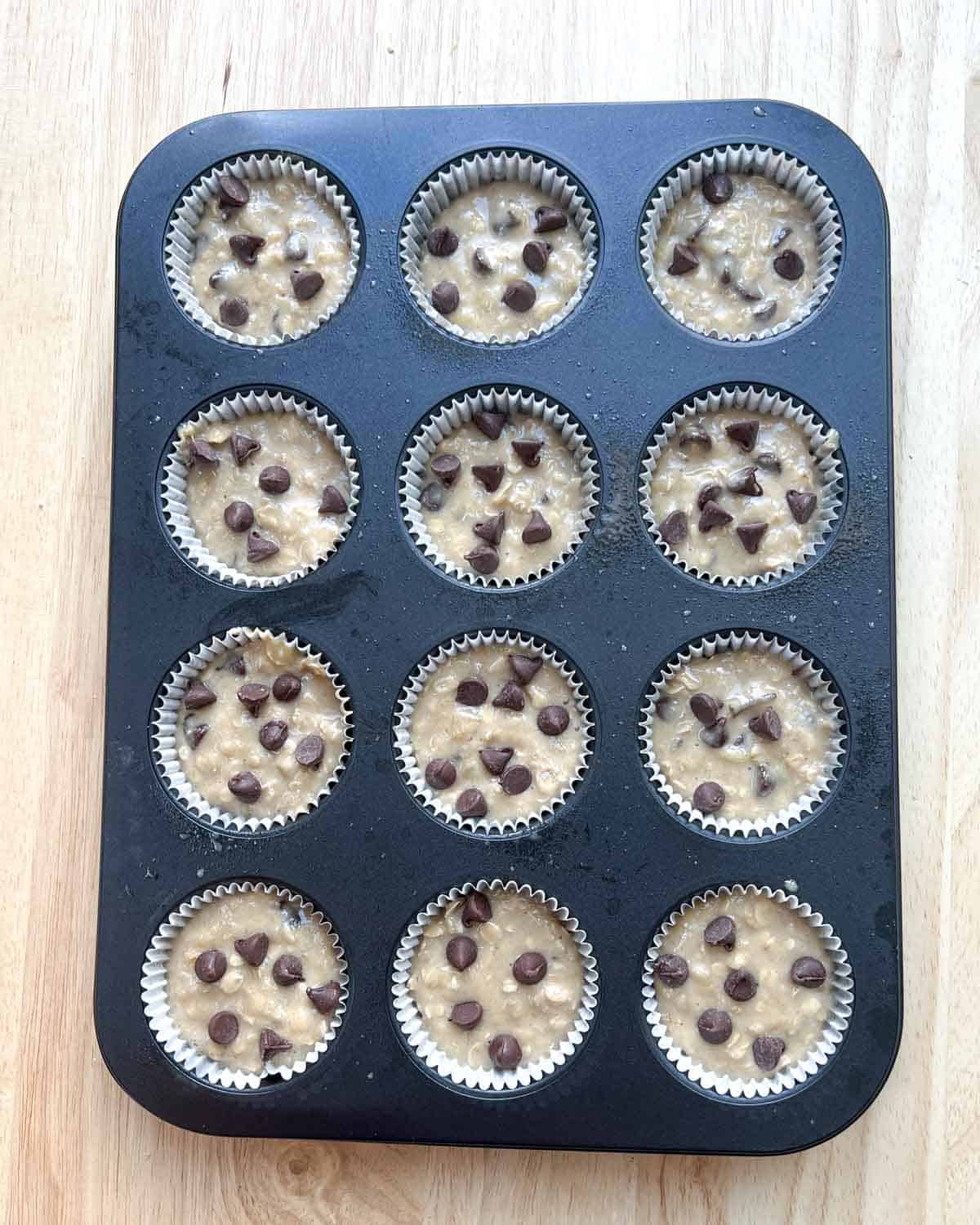 batter added to a muffin tin pan and topped with chocolate chips.