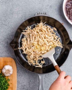 Shredded chicken being sautéed in a black skillet with a white spatula.